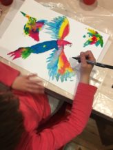 Enfant dessinant un oiseau très coloré.
